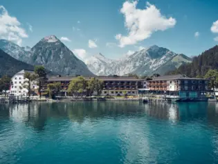 Das Fürstenhaus Hotel am Achensee mit umliegenden Bergen und Wolken am Himmel.