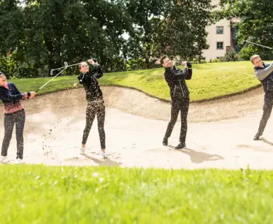 Group of people playing golf on a grassy field with trees in the background.