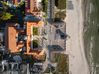 Gebäude an einem Strand mit einem Gehweg umgeben von Pflanzen und Bäumen aus der Vogelperspektive..