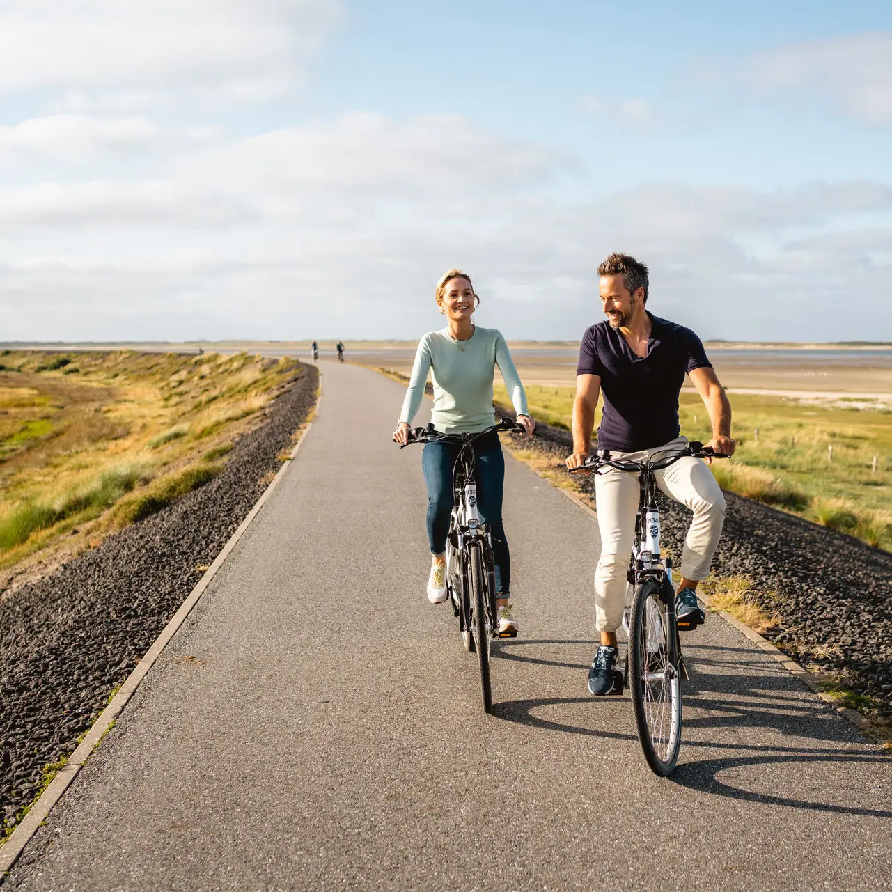Ein Mann und eine Frau fahren auf dem Sylter Deich Fahrrad.
