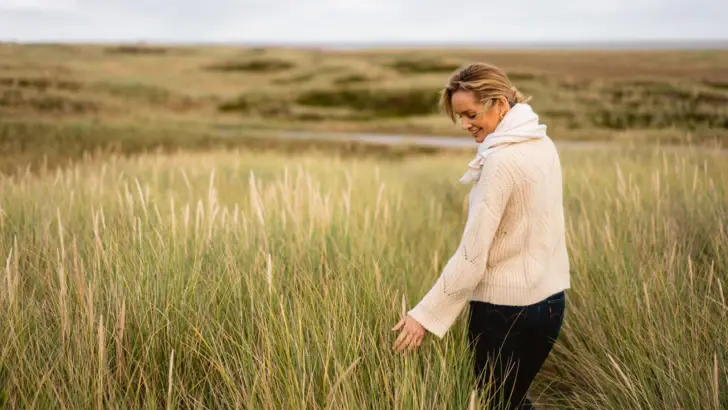 Frau steht in einem Feld mit hohem Gras.