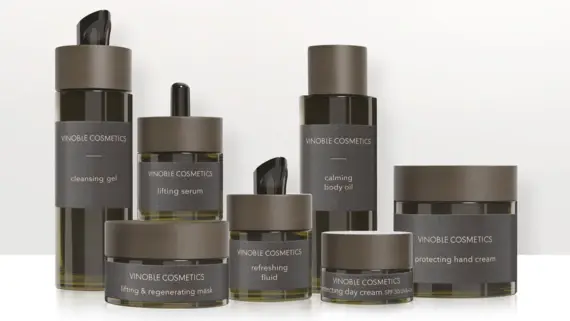 A collection of VINOBLE Cosmetics skincare products, presented on a light background. Various dark brown containers with transparent elements and black lettering can be seen, including a cleansing gel, a lifting serum, a soothing body oil, a refreshing fluid, a protective hand cream and a lifting & regenerating mask. All products are elegantly and uniformly designed and convey an image of luxurious cosmetics.