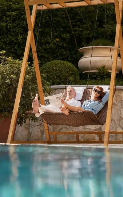 Mann und Frau liegen in einer Hängeschaukel am Poolrand.