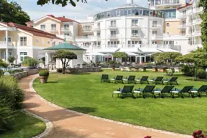 Liegestuhl im Garten mit Bäumen und klarem Himmel im Hintergrund.