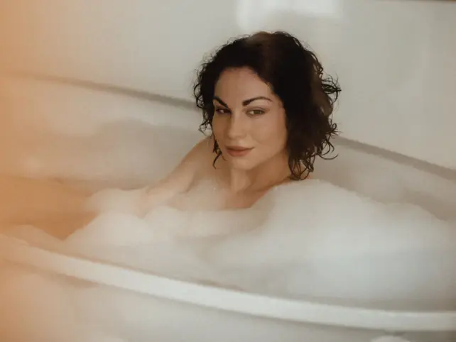 Eine Frau liegt in einer schaumigen Badewanne und entspannt. 
