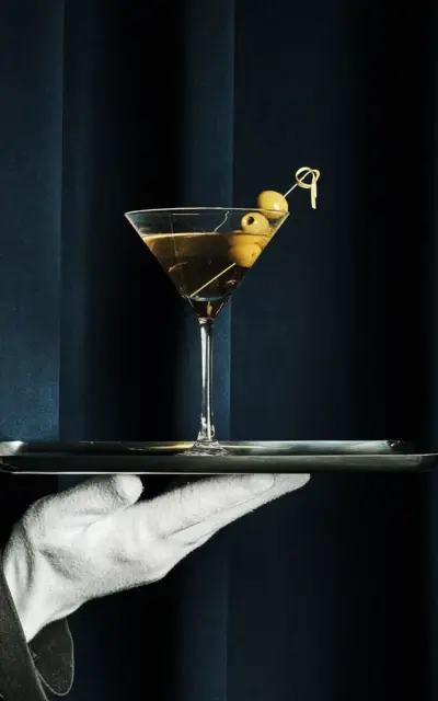 Eine Hand hält ein Tablett mit einem Martini-Glas.