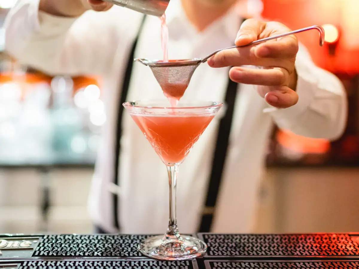 Ein Barkeeper gießt ein rotes Getränk in ein Martiniglas.