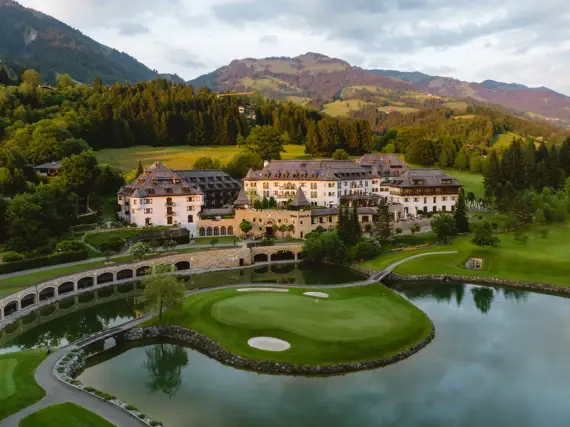 Großes Gebäude mit Golfplatz und See umgeben von Bäumen und Bergen.