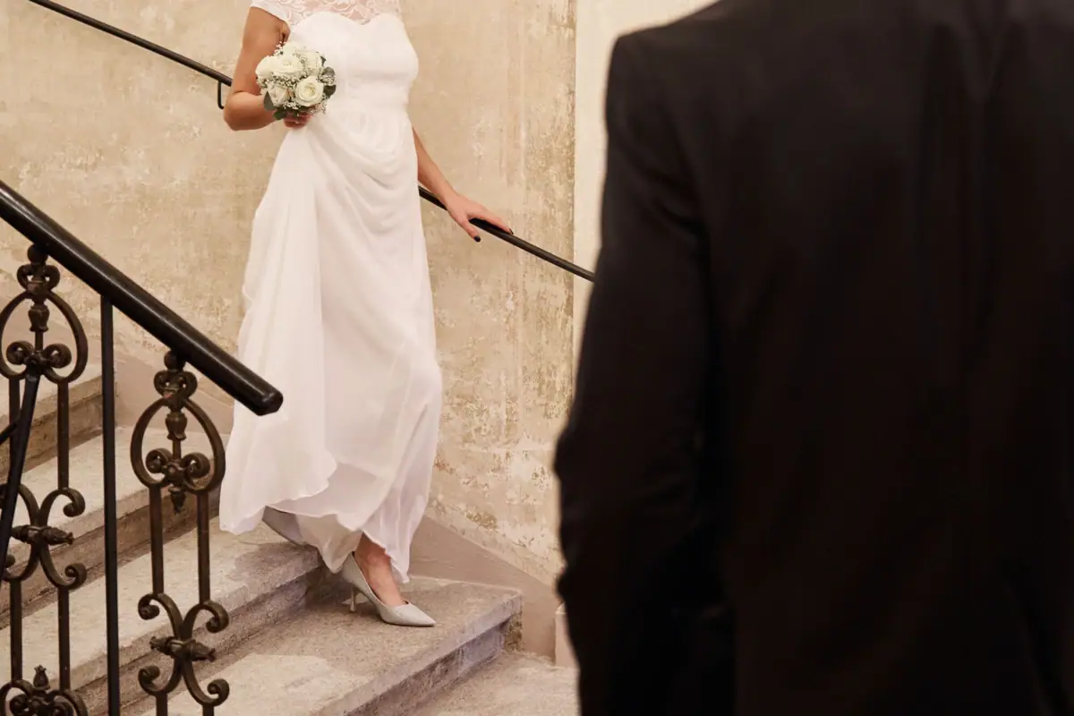 Eine Braut in einem weißen Kleid hält einen Blumenstrauß und steigt Treppen hinauf.