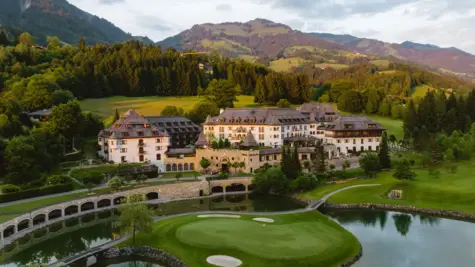 Das A-ROSA Kitzbühel mit einem Golfplatz und einem See, umgeben von Bäumen und Bergen.