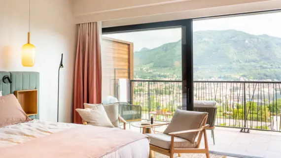 Bedroom with a mountain view, featuring a neatly made bed, elegant furnishings, and large windows.