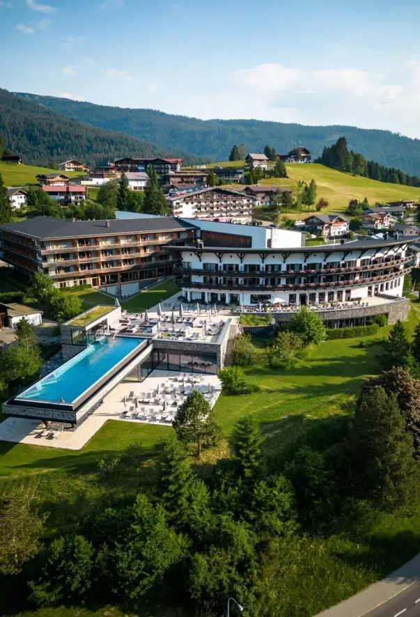 Ein Gebäude mit einem Infinity Pool inmitten eines Bergdorfs, umgeben von Bäumen und Grünflächen.