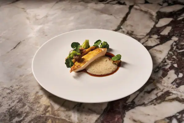 Ein weißer Teller mit einem Gericht darauf steht auf einem marmorierten Untergrund.