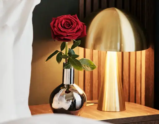 Eine Rose in einer Vase neben einer Lampe.