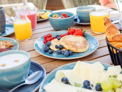 Una tavola da colazione riccamente imbandita con pancake e frutti di bosco freschi al centro.