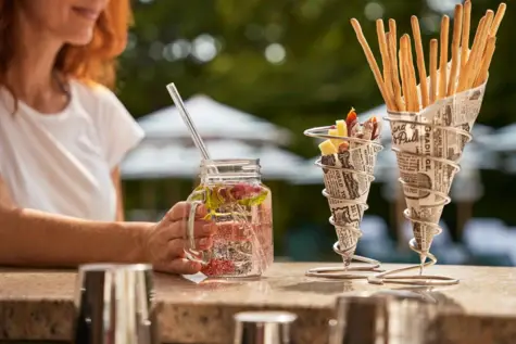 Frau hält ein Glas Wasser an einem Tisch im Freien.
