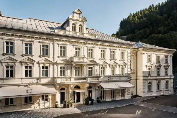 Außenansicht des historischen Straubinger Grand Hotel in Bad Gastein bei Tageslicht, umgeben von Bergen und Wald. Eindrucksvolle Architektur der Belle Époque in stilvoller Kulisse.