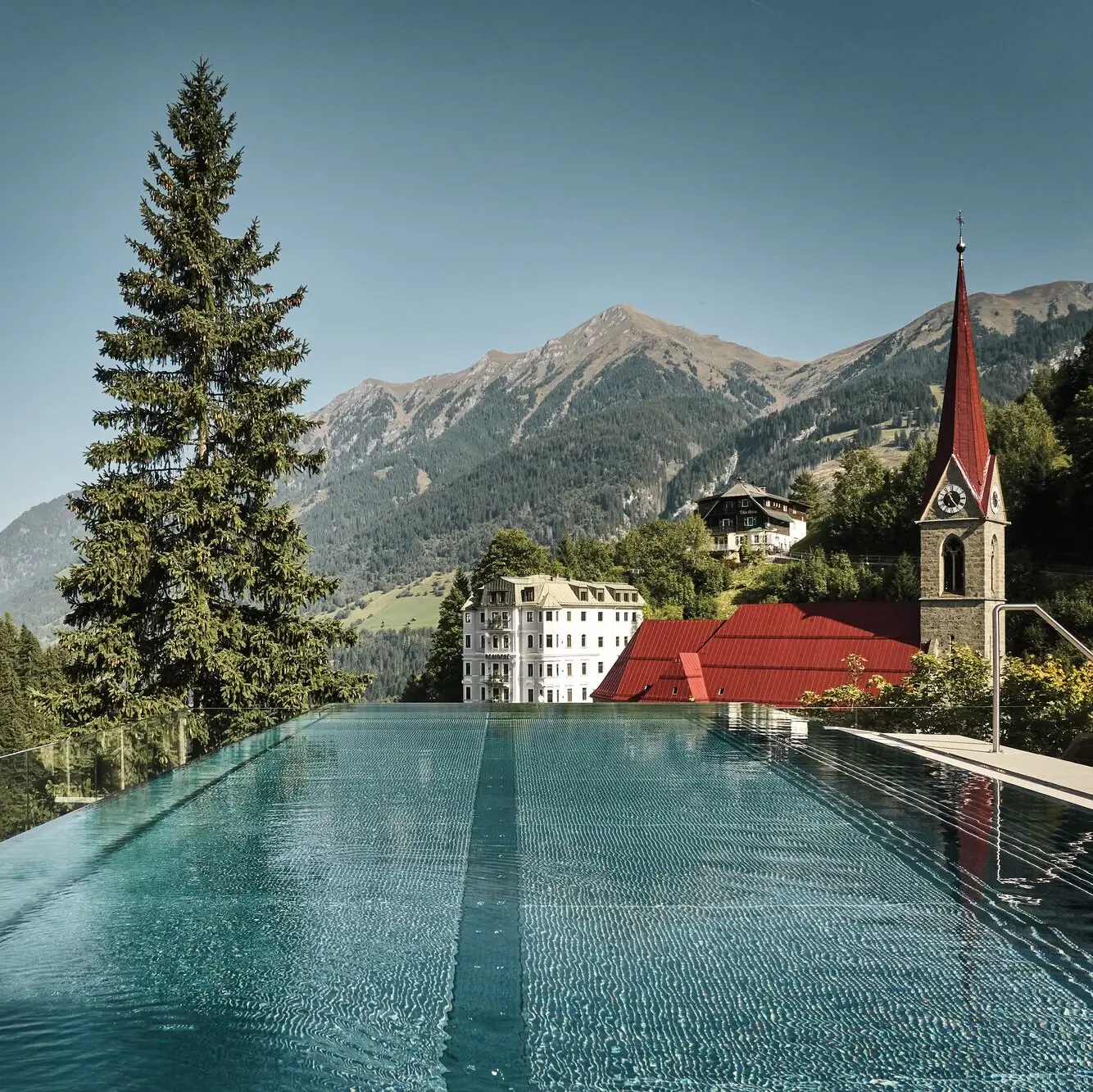 Pool im Vordergrund, dahinter eine Kirche und eine Bergkette