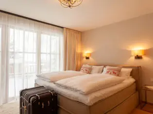 Ein beiges Polsterbett steht an einer weißen Wand mit weißer Bettwäsche und zwei weihnachtlichen Dekokissen mit Rentieren darauf.
