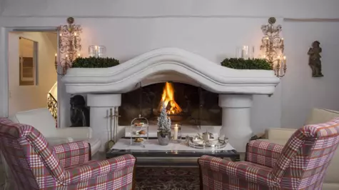 Two cozy armchairs stand in front of an open fireplace and tea time is served on the table.
