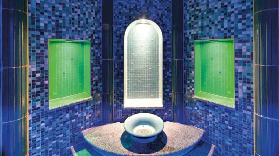 Farbig beleuchtetes Dampfbad mit türkis-blauen Mosaikfliesen und zentralem Wasserbecken im A-ROSA Ostseehotel Kühlungsborn – ein Ort für tiefe Entspannung und wohltuende Wärme