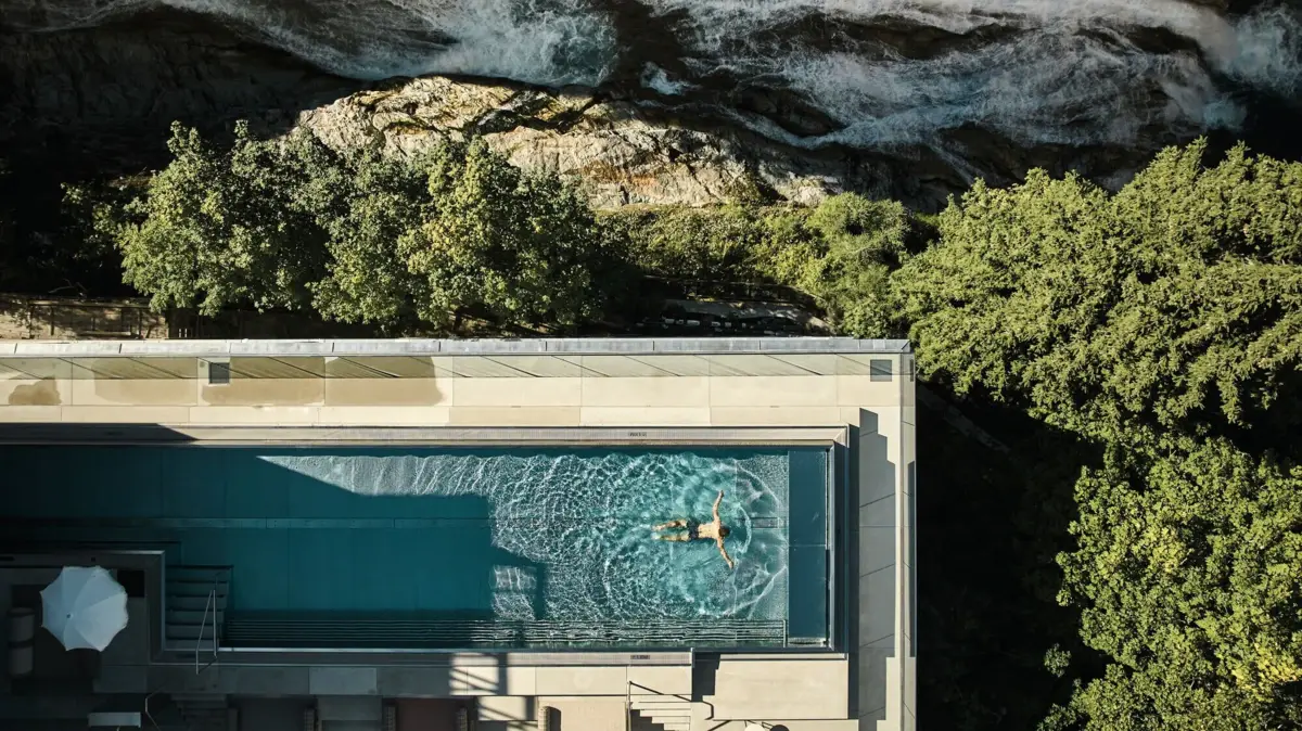 Perfektion in einem Poolbild Vogelperspektive eines Poolbildes in dem jemand schwimmt, neben einem Wasserfall, Felsen und Landschaft