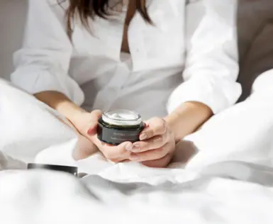 Person holding a jar of cream in an interior space.