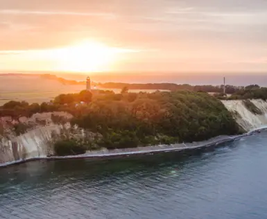 Ein Leuchtturm auf einem Hügel neben einem Gewässer bei Sonnenuntergang.