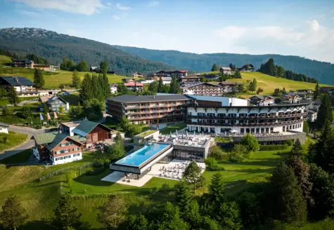 Gebäude mit Infinitypool in einem Bergdorf, umgeben von Bäumen und Graslandschaft.