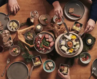 Rustikales Abendessen mit alpiner Jause: verschiedene Käsesorten, Wurst, Brot, Aufstriche und eingelegte Spezialitäten werden auf einem Holztisch stimmungsvoll angerichtet und gemeinsam genossen.