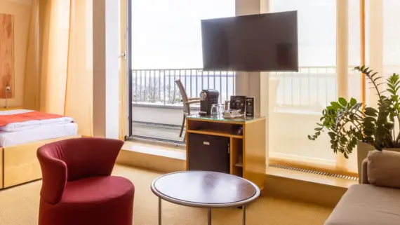 Ein Hotelzimmer mit einem roten Sessel, einer Kaffeemaschine und einer großen Dachterrasse.
