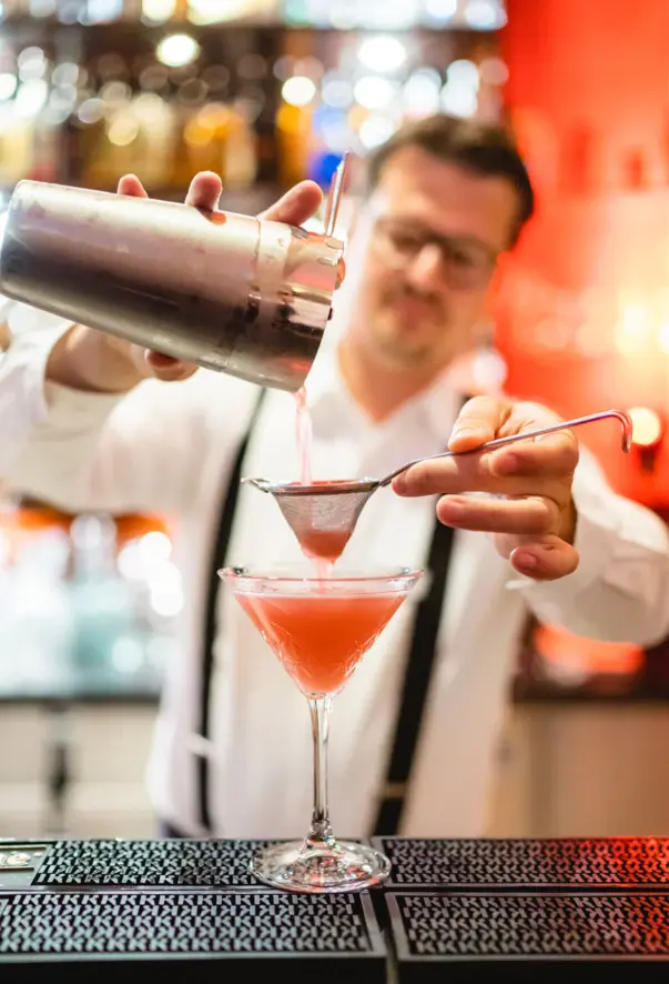 Ein Baarkeeper schenkt einen Cocktail in ein Glas.