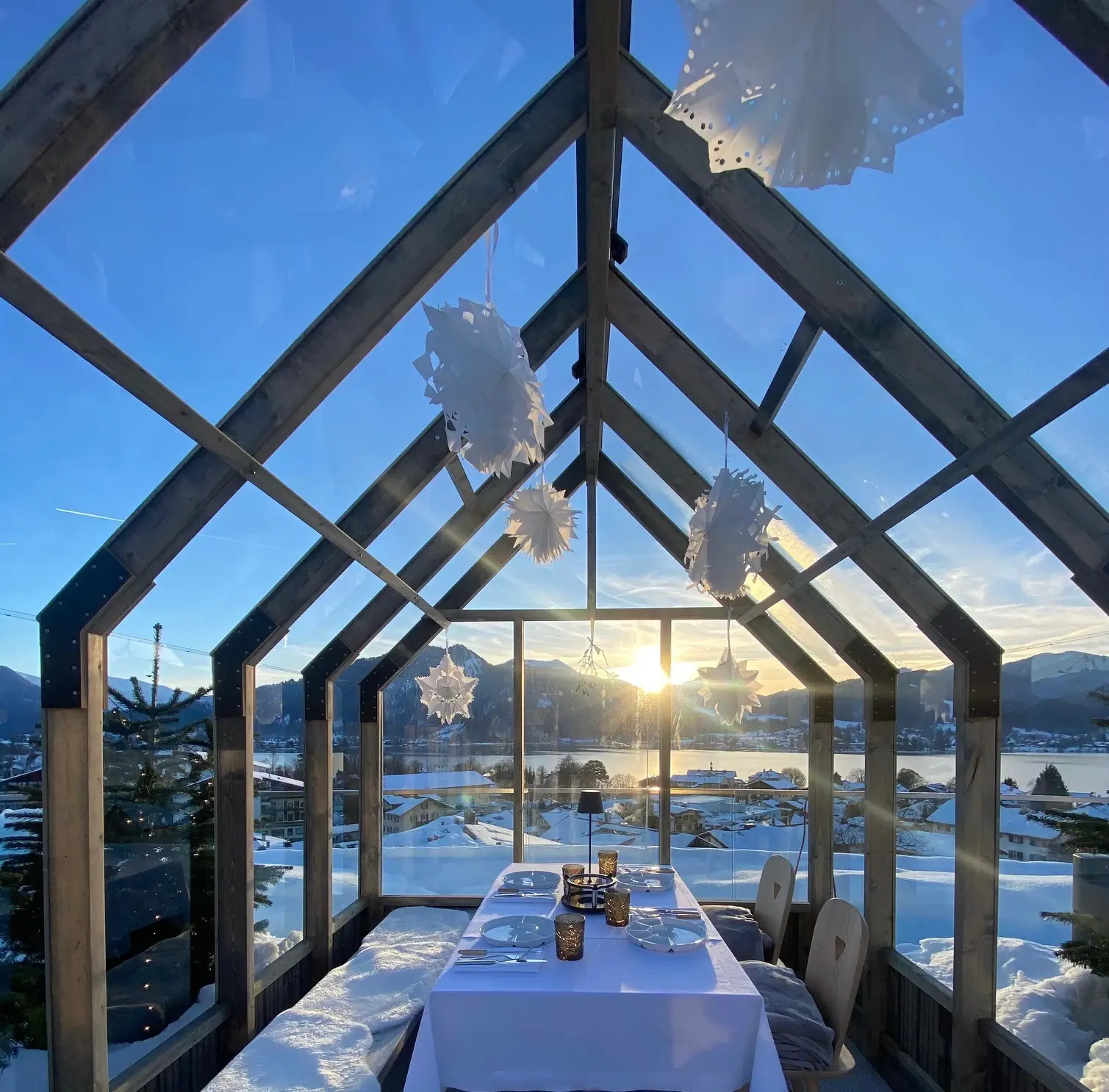 Ein Tisch mit Stühlen unter einem Glasdach, im Hintergrund Schnee und Berge.
