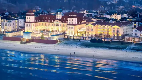 Beleuchtetes großes Gebäude am Strand mit Wasser im Vordergrund.