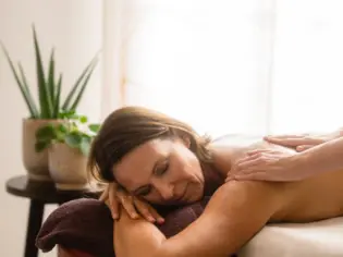 A relaxing wellness massage in a spa setting, where a masseuse's hands gently glide over the back of a woman lying on a massage table.