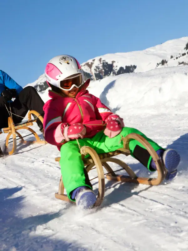 Ein Mann und ein Mädchen rodeln einen schneebedeckten Hang hinunter.