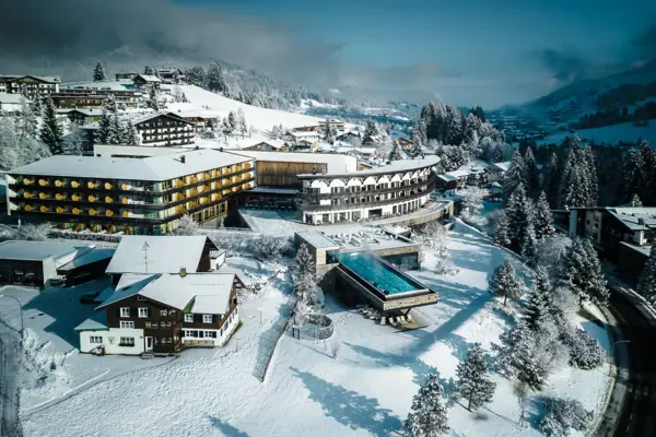 Verschneite Landschaft mit dem A-ROSA Ifen Hotel Kleinwalsertal und Bäumen.