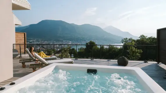 Frau sitzt auf einer Terrasse mit einem Whirlpool, der auf eine Stadt blickt.