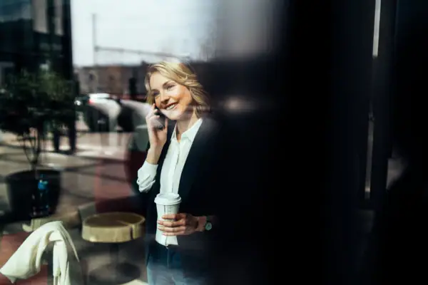 Eventservice Eine Frau hält eine Kaffeetasse und telefoniert mit einem Handy.