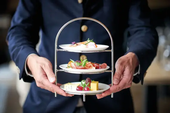 Person hält ein dreistöckiges Tablett mit Essen.