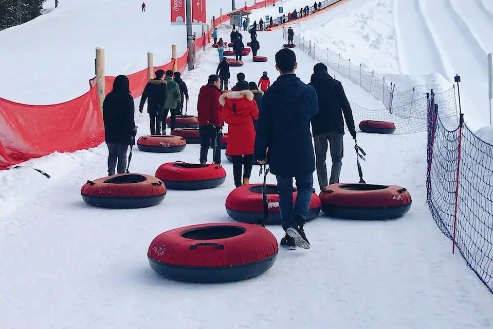 Tube Park Schnee Eine Gruppe von Menschen ziehen rote Schwimmreifen für Schneerutschen hinter sich her.
