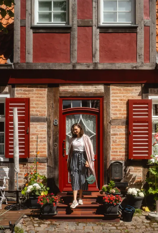 Eine Frau steht vor einer Lübecker Altstadtfassade mit roter Tür und roten Fensterläden. 