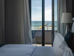 Innenansicht eines Hotelzimmers mit einem Bett und Meerblick durch das Fenster.