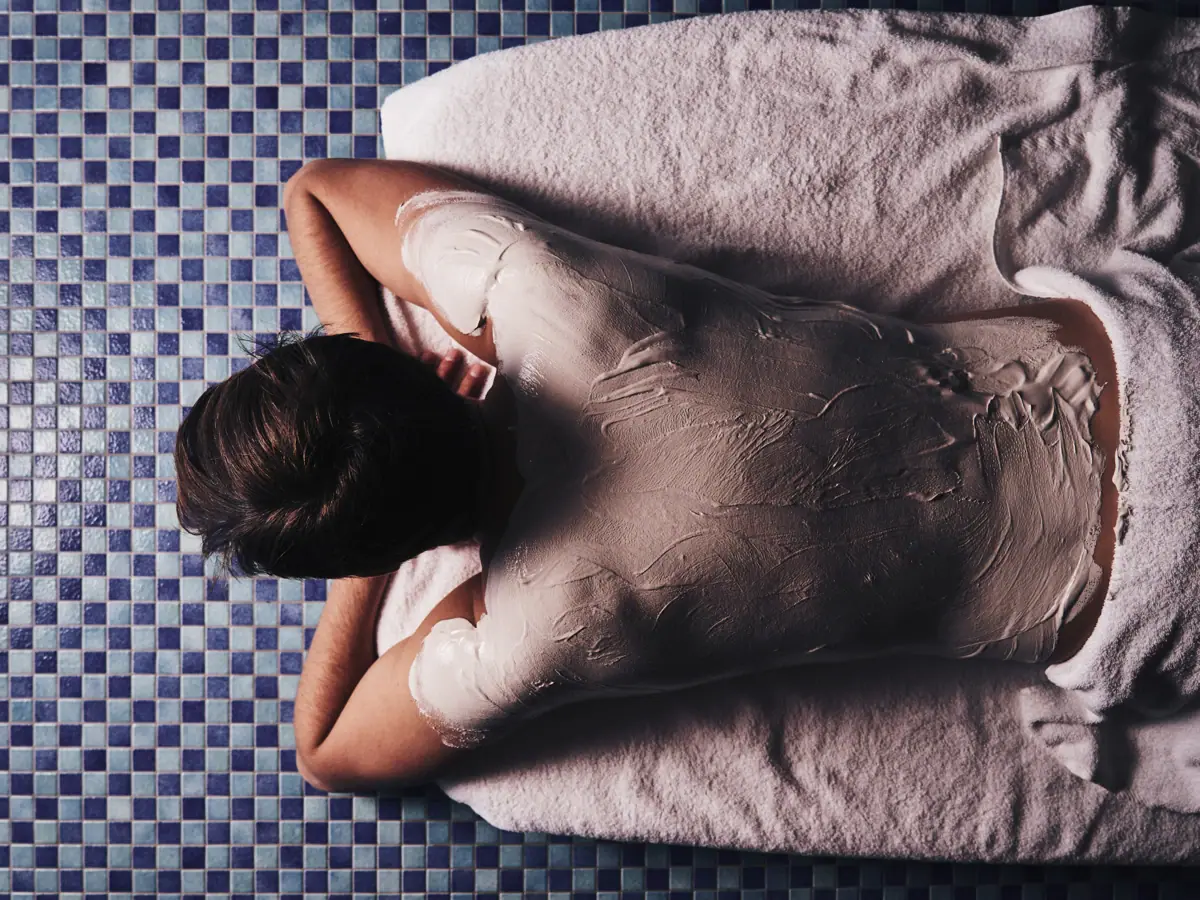 Eine Person liegt auf einem weißen Handtuch mit weißem Körper, der mit Schlamm bedeckt ist.