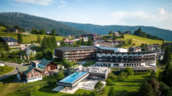 Gebäude mit einem Infinity-Pool inmitten eines Bergdorfes, umgeben von Bäumen und einer Landschaft mit Bergen.