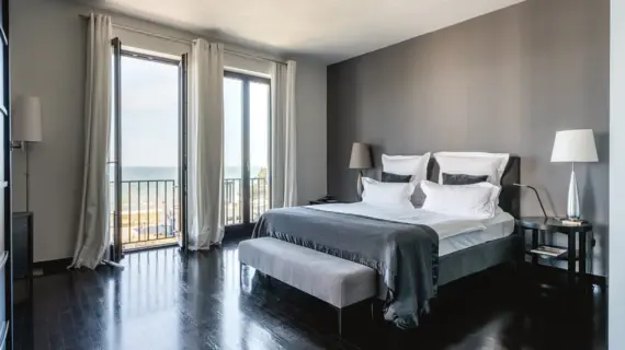 Schlafzimmer mit großem Fenster mit Blick auf das Meer, ausgestattet mit einem komfortablen Bett und stilvoller Einrichtung.