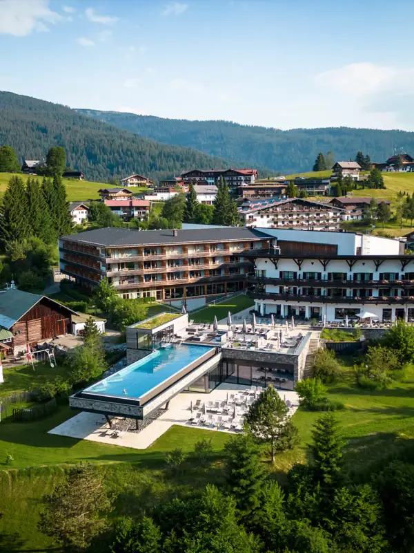 Das A-ROSA Ifen Hotel Kleinwalsertal aus der Vogelperspektive mit einem Pool und Bergen im Hintergrund.