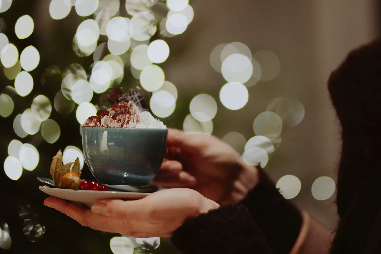 Eine Person hält eine Tasse mit einer heißen Schokolade mit Sahne.