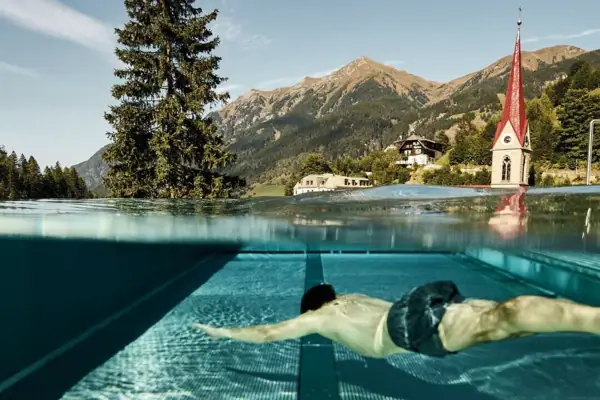 Ein Mann schwimmt in einem Pool mit Bergen im Hintergrund.