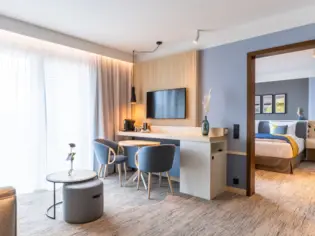 Ein großes Hotelzimmer mit einem Wohnbereich inklusive Schreibtisch und Sofa mit Blick in den Schlafbereich.